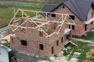 Unfinished brick house with wooden roof structure under construction.