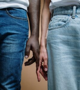 Two people holding hands with fingers interlaced, seen from the waist down in denim jeans.