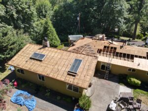 Aerial view of a house under construction with workers on the partially rebuilt roof and piles of lumber nearby.