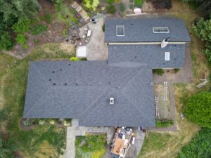 Aerial view of a large gray-roofed house with a backyard patio and a pile of building materials nearby.