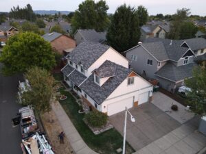 Aerial view of a residential neighborhood with grey shingle roofs, trees, and a garbage truck parked on the street to the left.