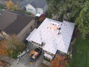 Aerial view of a residential roof under construction with underlayment, plywood, and scattered materials on a multi-story home
