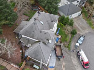 Aerial view of a suburban house with workers on the roof repairing shingles, with tools and trucks nearby and a trampoline in the backyard.
