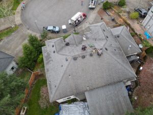 Aerial view of a rooftop construction site with workers on the roof and trucks parked on the street below.