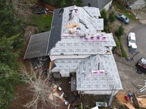 Aerial view of a house under construction with workers on the sloped roof and scattered building materials and insulation wrap around it.