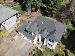 Aerial view of two gray-roofed houses with fenced backyards, trees, and a mix of lawns and gravel.